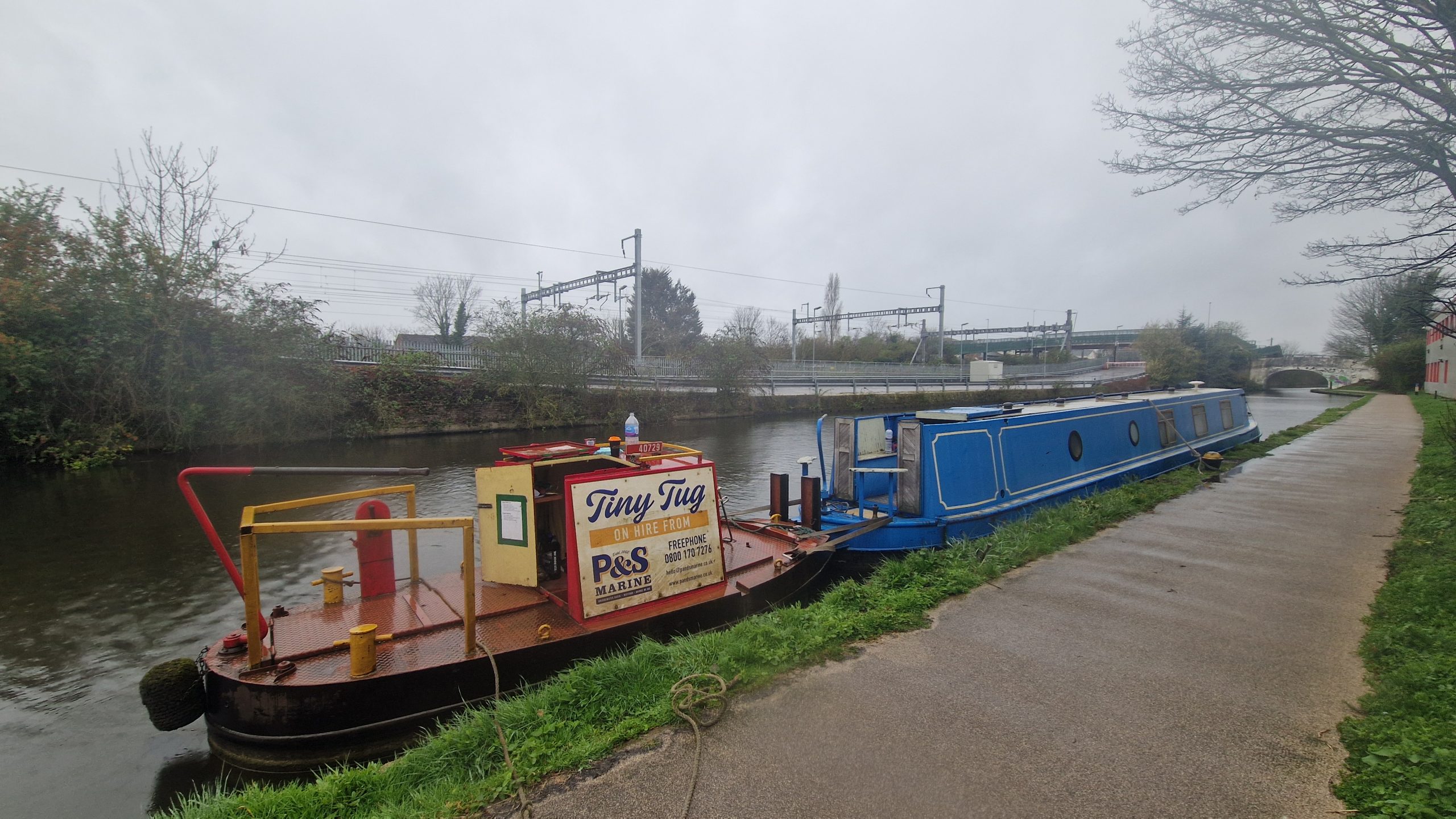 non-running narrowboat being moved with tug assistance on UK canal